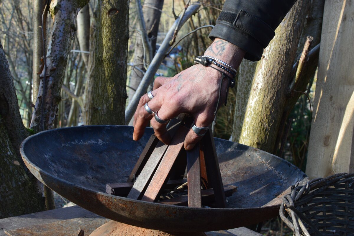 Eine Hand legt Holz in eine Feuerschale im Wald