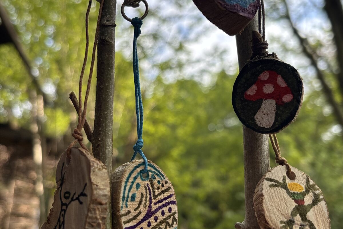 Bemalte Anhänger aus Holz hängen zwischen Ästen im Wald